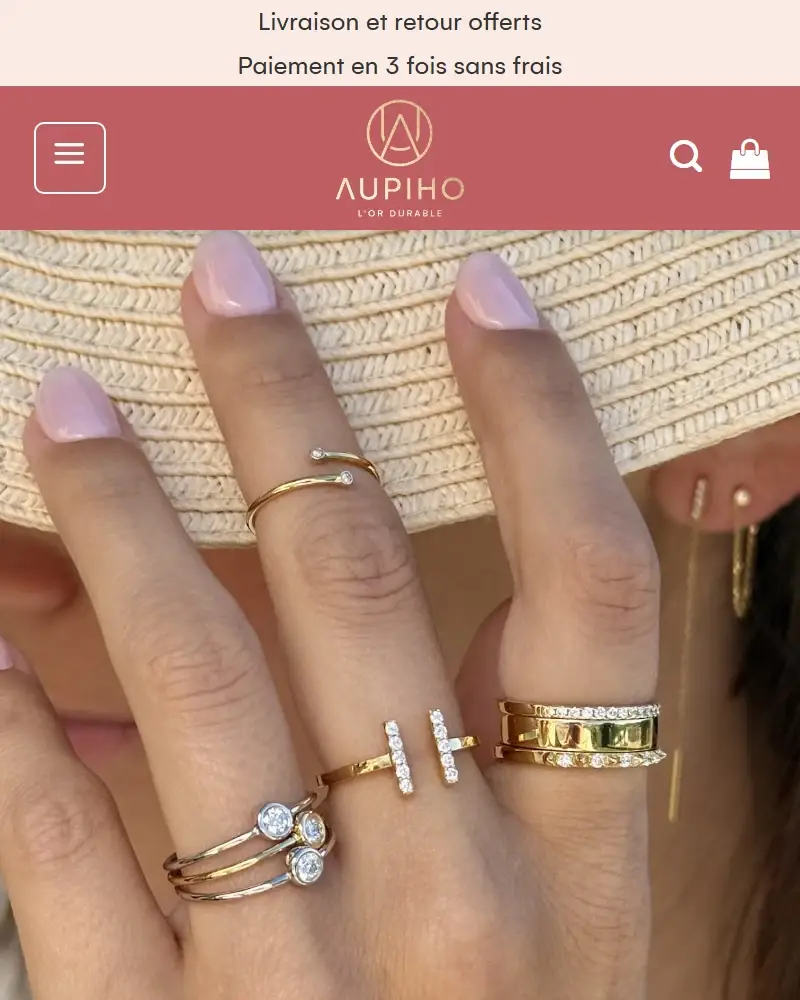 Version mobile de l’accueil d’aupiho.com : logo AUPIHO sur fond rose et visuel de bagues en or.