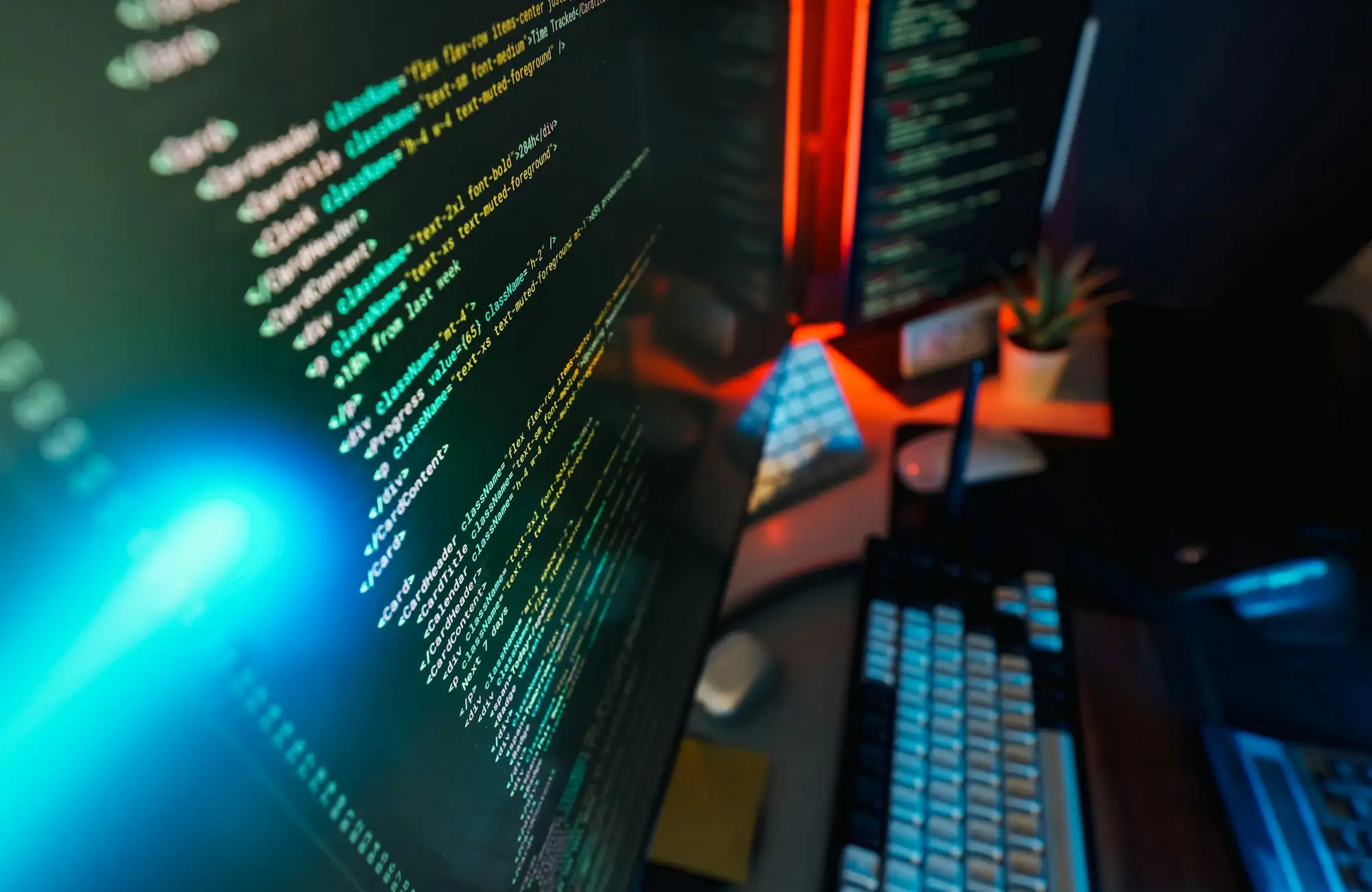 Écrans affichant du code et un terminal, clavier et plante sur le bureau.