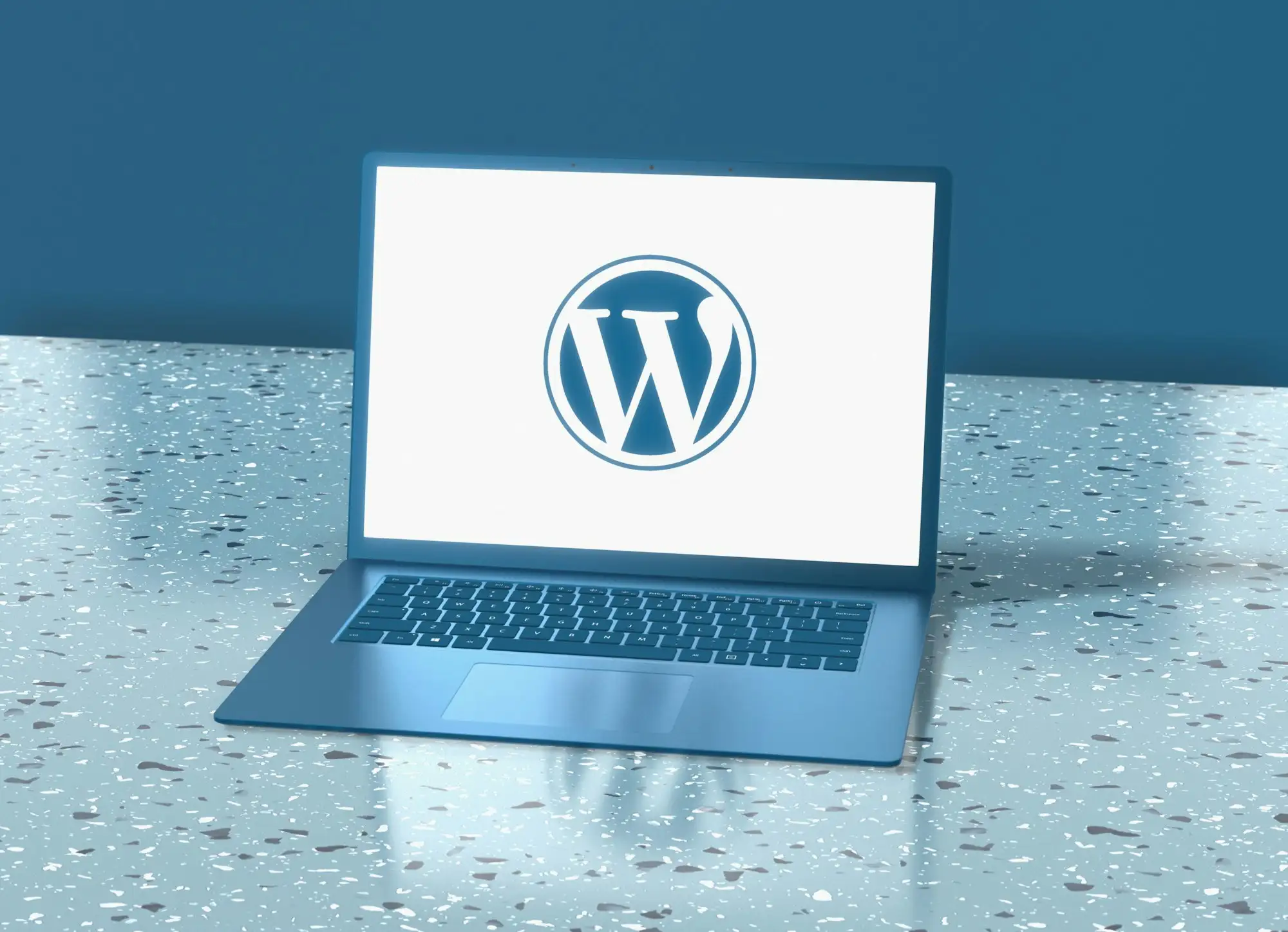 Ordinateur portable affichant le logo WordPress, sur un plan de travail bleu.